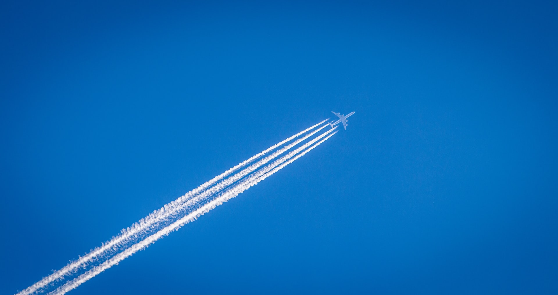 A passenger jet leaves a contrail against a bright blue sky