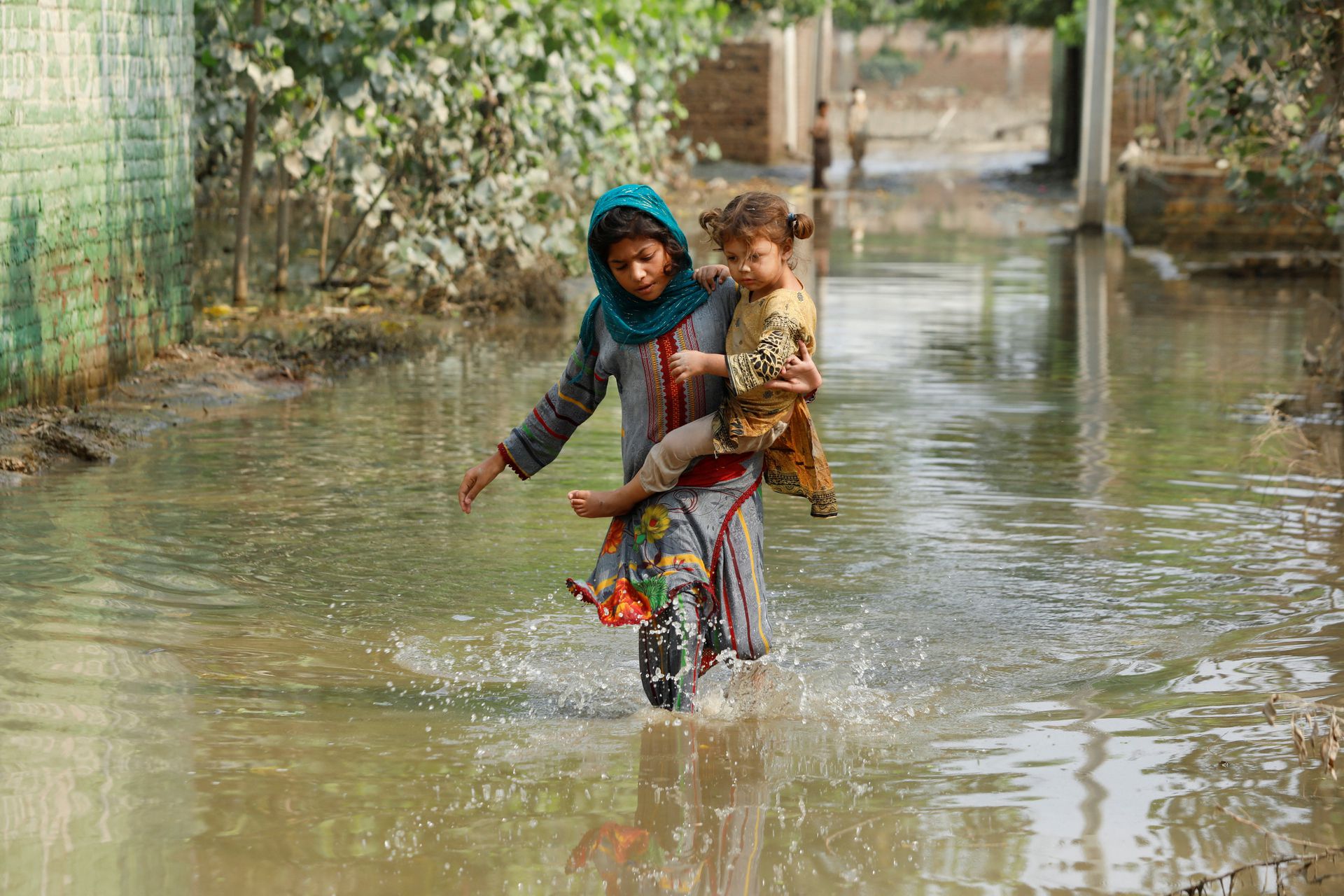 A girl carries her sibling as she walks through stranded flood water, following rains and floods during the monsoon season in Nowshera, Pakistan September 4, 2022. REUTERS/Fayaz Aziz