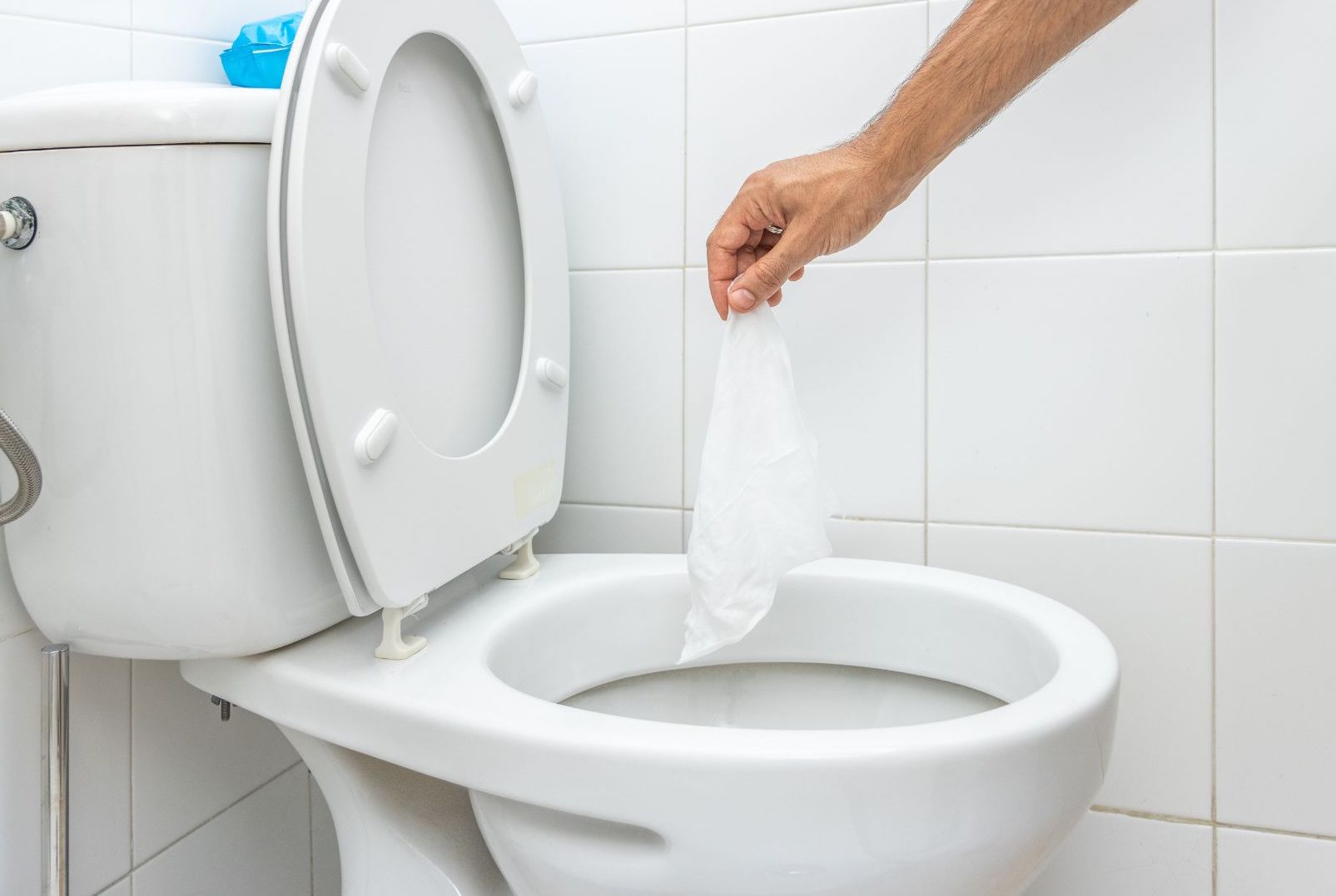 A toilet with the seat open. An arm is extended over the toilet holding a wet wipe.