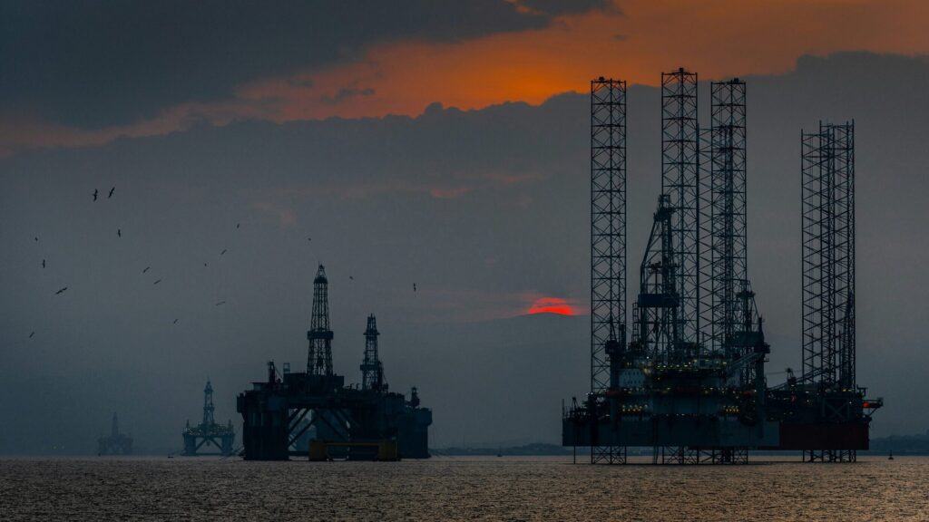 Two oil rigs at sea with the sun setting in the background.