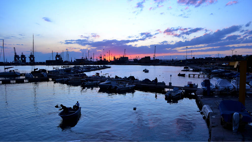 A view of Taranto at sunrise with cranes from the Ilva factory visible in the background