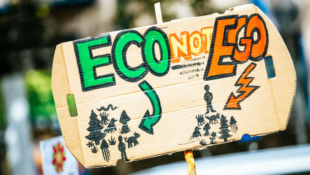 A sign that says "Eco not Ego." Underneath, eco is pointing to an illustration of a person stood amongst nature. Under ego, a person is stood above nature.