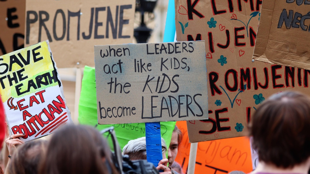 At a climate cation march, a central sign says "when leaders become kids, the kids become leaders."